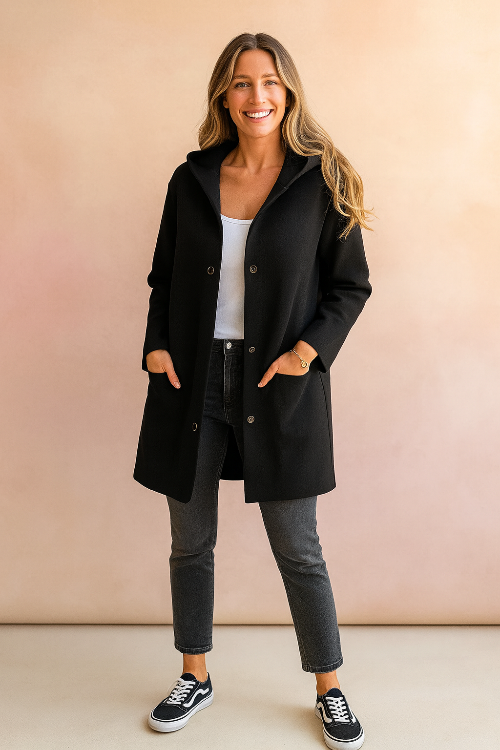 Black hooded button-up coat with long sleeves, front pockets, and straight cut, styled with dark slim-fit jeans, white tank top, and black low-top sneakers.