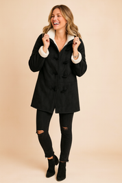 Black duffle coat with white sherpa lining, toggle buttons, and front seam detailing, styled with distressed black jeans and suede ankle boots for a casual winter look.