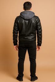 Back view of a black leather biker jacket with gray hood insert, ribbed hem and cuffs, and shoulder epaulets, styled with black trousers and sneakers.