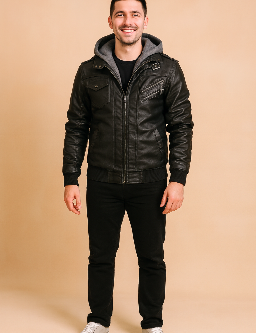 Black leather biker jacket with zip closure, multiple pockets, shoulder epaulets, and gray hood insert, styled with black trousers and gray sneakers.