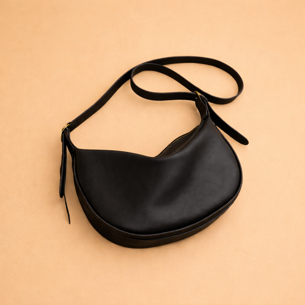 Premium black leather crescent shoulder bag featuring a sleek curved shape, refined finish, and adjustable strap for a modern, timeless look.