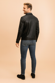 Black leather jacket with structured stitching and smooth matte finish, styled with slim blue jeans and black suede ankle boots, shown from the back view.