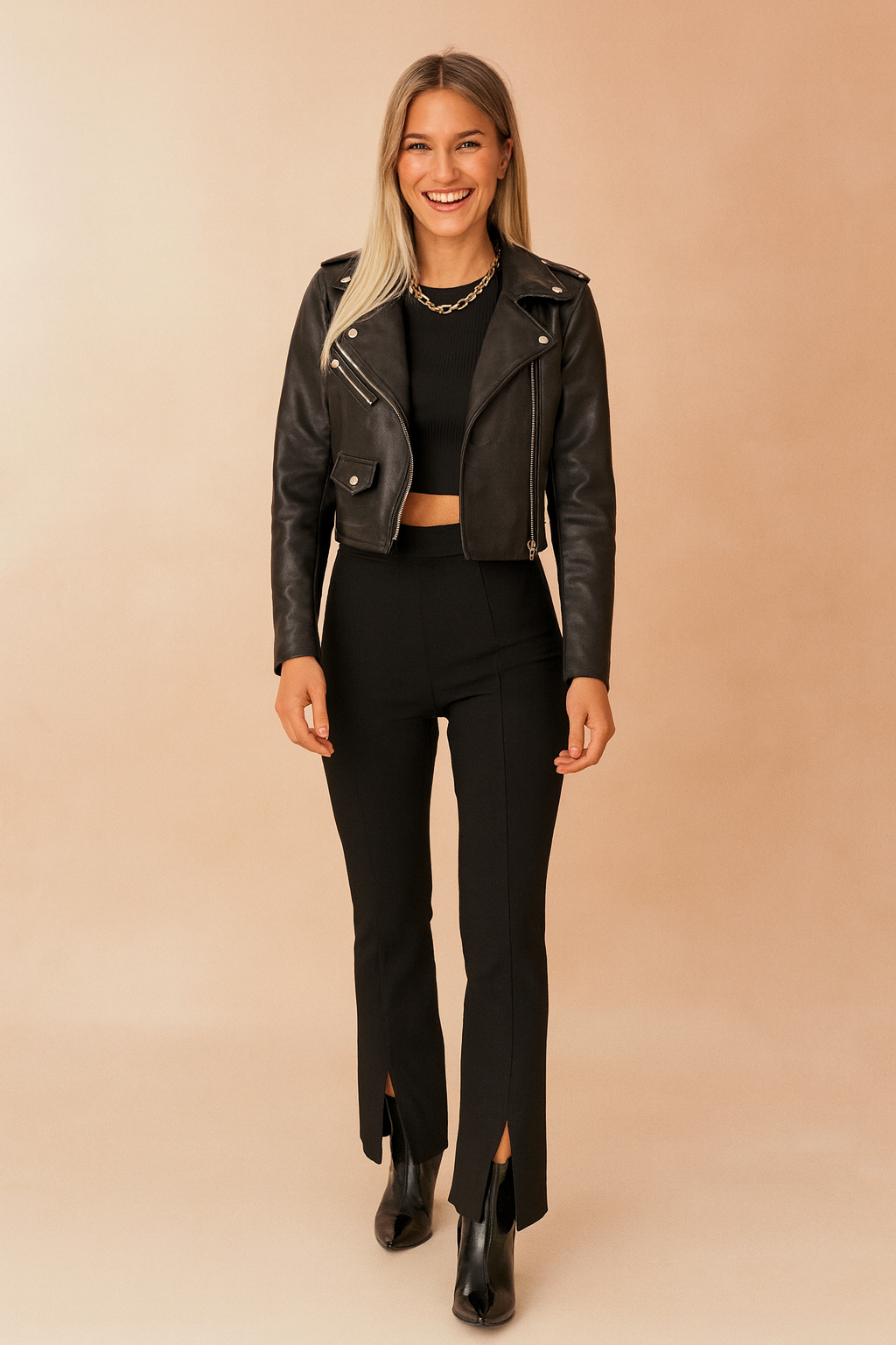 Black cropped leather biker jacket with silver zippers, paired with a fitted black crop top, high-waisted slit-hem trousers, and black ankle boots.
