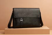 Black faux leather messenger bag with flap closure, front strap and silver H-buckle detail, displayed on a beige gradient background.