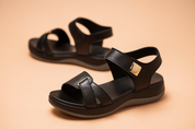 Black leather sandals with cushioned soles, gold-tone side buckle detail, and wide dual straps, designed with a contoured footbed and sporty black-and-white outsole.