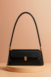 Black leather shoulder bag with gold clasp and structured top handle, displayed on a soft sand-toned platform with warm gradient lighting.