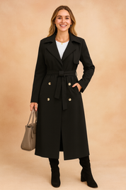 Black long trench coat with double-breasted gold buttons, belted waist tie, notch lapels, and side pockets, styled with a white inner top, black knee-high suede boots, and a taupe structured handbag.