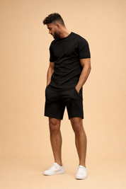 Minimalist black short-sleeve fitted t-shirt paired with matching black tailored shorts, smooth matte fabric finish, clean seams, modern slim silhouette, monochrome men’s casual set with black low-profile 