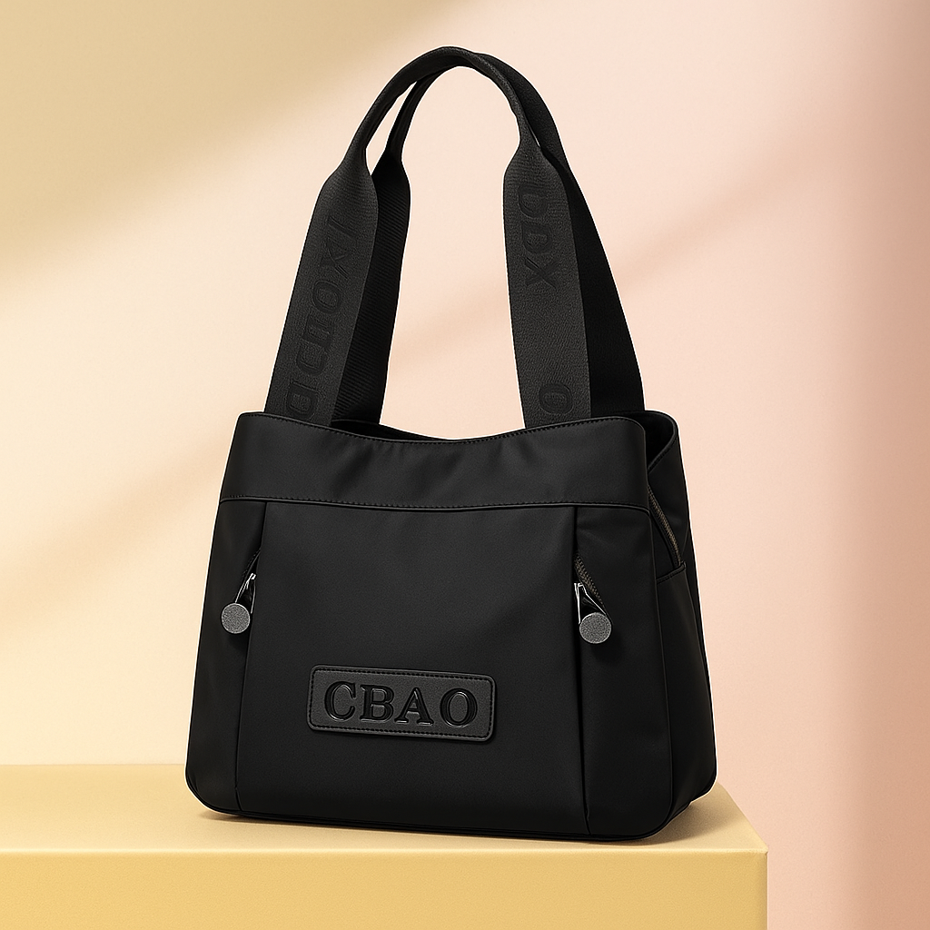 Black nylon shoulder bag with wide embossed logo straps, dual front zippers, and a stitched CBAO patch, presented on a neutral platform with a warm sand and pastel pink gradient background.