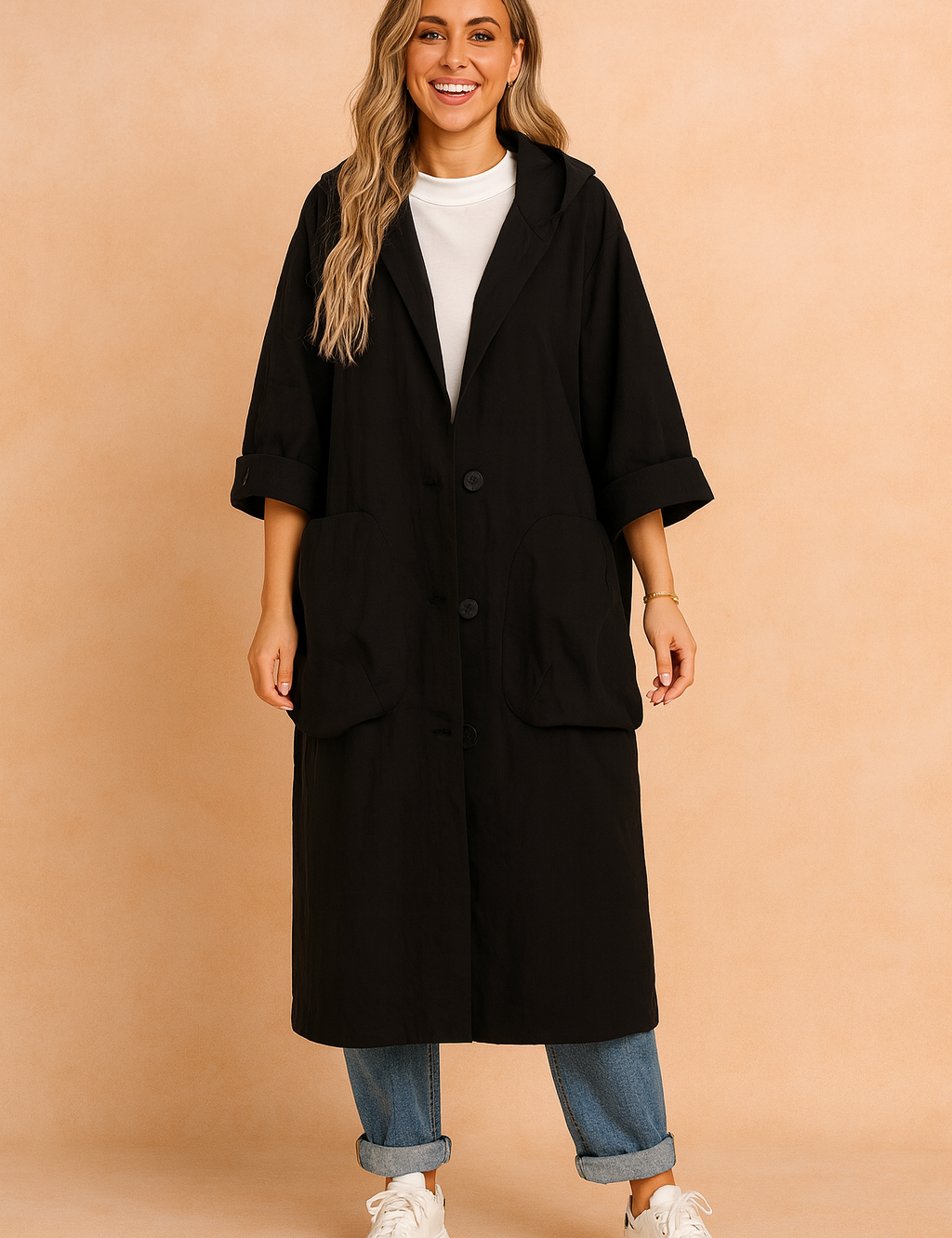 Black oversized button-down coat with wide lapels, large front pockets, and rolled sleeves, styled over a white high-neck top, cuffed blue jeans, and white sneakers.