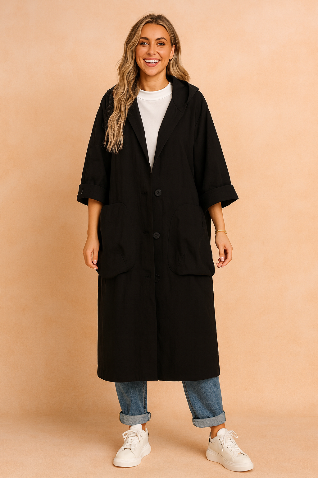 Black oversized button-down coat with wide lapels, large front pockets, and rolled sleeves, styled over a white high-neck top, cuffed blue jeans, and white sneakers.