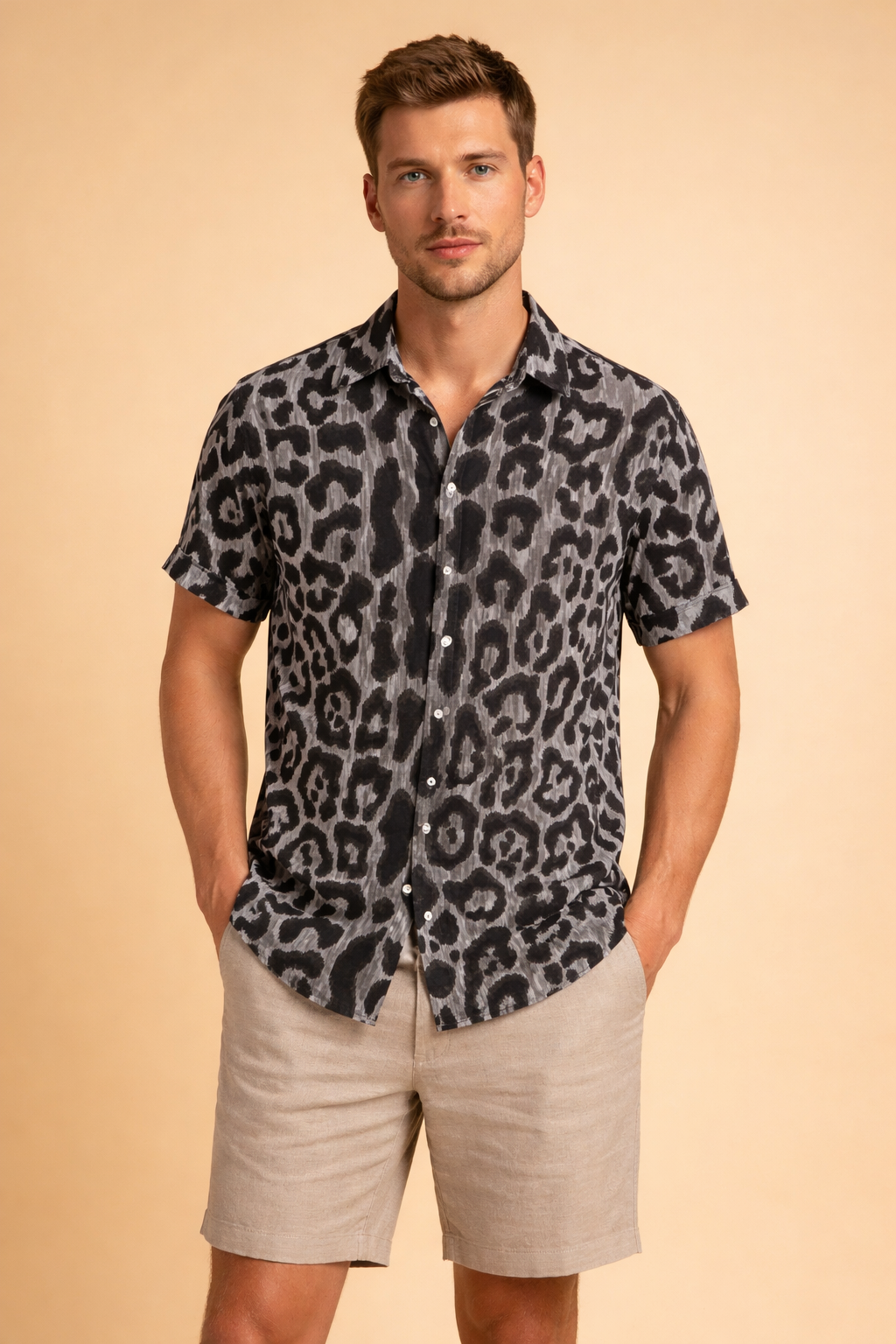 Short-sleeve black button-up shirt with intricate beige and olive paisley pattern, classic collar, straight hem, paired with light beige tailored shorts featuring a clean flat front and knee-length cut.
