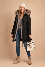 Black winter parka jacket with faux fur hood, front zipper and snap button closure, large flap pockets, adjustable waist drawstring, paired with slim blue jeans and black ankle boots.