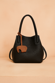 Black pebbled leather tote bag with white stitching, double handles, and a brown elephant-shaped charm.