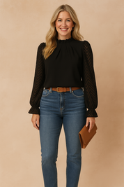 Elegant black blouse with structured pleats and sheer chevron-patterned long sleeves, paired with high-waisted blue jeans and a tan belt.