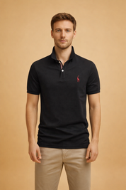 Black short-sleeve polo shirt with structured collar, two-button placket featuring subtle contrast trim, and a small embroidered chest logo, styled with tailored straight-leg trousers for a clean, modern outfit.