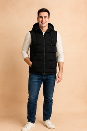 Men’s black quilted puffer vest with hood, zip closure, and two zippered pockets, paired with casual jeans and sneakers for a modern, sporty look
