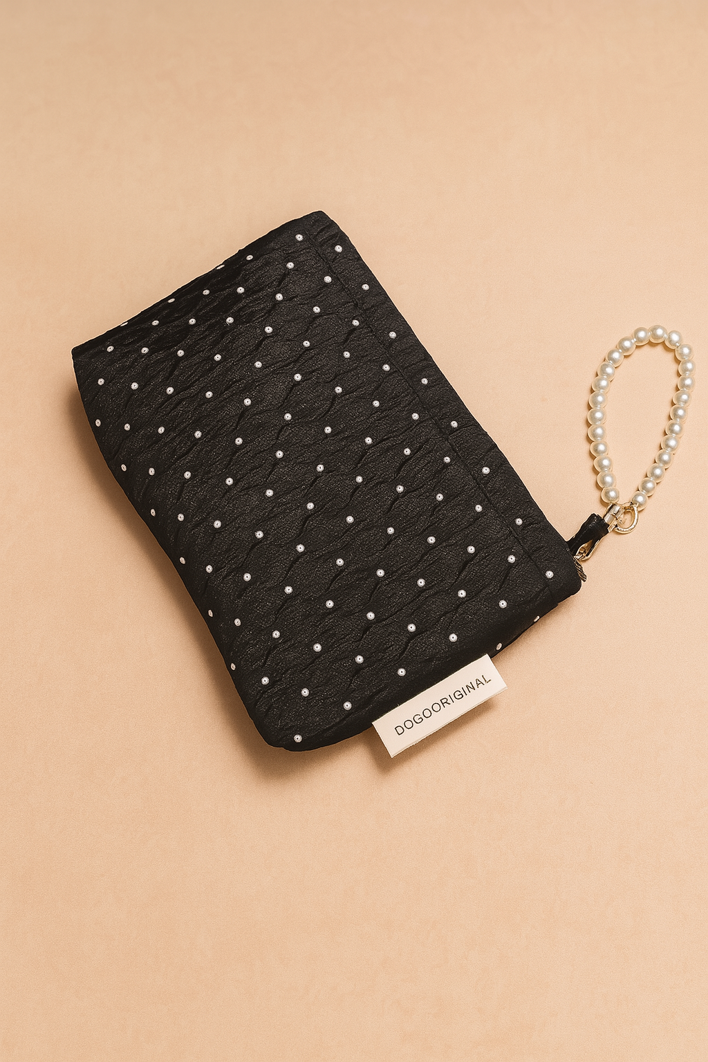 Black quilted clutch with a pearl dot pattern and a pearl-beaded wrist strap, featuring a visible branded fabric tag and elegant textured fabric.