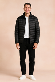 Black puffer jacket with horizontal quilted design and front zipper, styled with a white t-shirt, black trousers, and white sneakers.