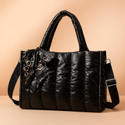 Black quilted puffer tote bag with chain-print scarf, vertical stitching, top handles, and adjustable shoulder strap.