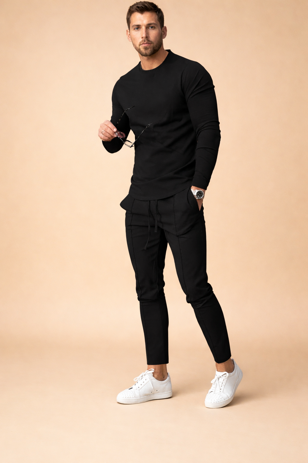 Slim-fit black long-sleeve crewneck shirt paired with tailored black tapered pants featuring structured seam detailing, styled with clean white low-top sneakers for a modern minimalist menswear look.