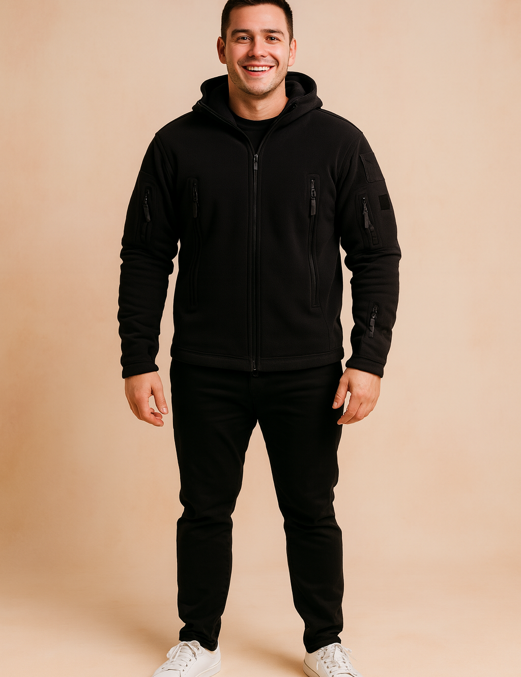 Black softshell tactical jacket with multiple zippered pockets and hood, styled with black trousers and white sneakers.