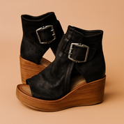 Black wedge sandals with distressed suede texture, wide front coverage, chunky wooden platform soles, and large oxidized silver buckles at the ankle.
