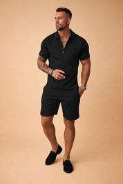 Black two-piece men’s summer outfit featuring a textured short-sleeve zip-neck polo shirt with geometric woven pattern, paired with matching tailored black shorts in the same structured fabric for a coordinated modern look.