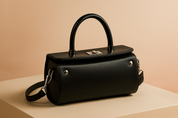 Sleek black rectangular handbag with a top handle, smooth leather texture, silver turn-lock clasp, and minimal metal button accents on each side, displayed on a neutral platform with soft fashion lighting.