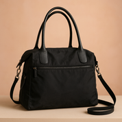 Black structured tote bag with dual top handles, a wide zippered front pocket, and smooth nylon-like finish with textured leather accents