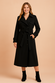 Elegant black double-breasted trench coat with belted waist, structured lapels, and long sleeves with buckle details, styled for a polished and sophisticated look.