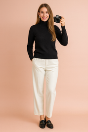 Black turtleneck sweater with long sleeves, paired with white tailored trousers and black leather loafers.