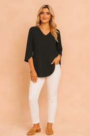 Black V-neck blouse with three-quarter sleeves paired with fitted white trousers and tan block sandals.