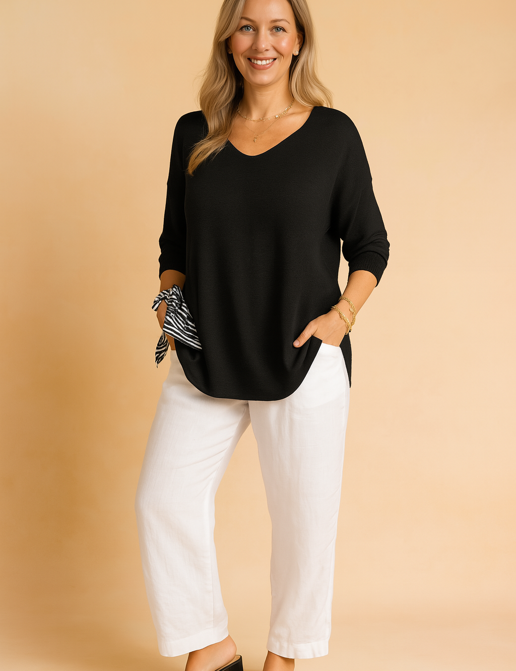 Black V-neck long-sleeve blouse with relaxed fit, paired with white straight-leg linen trousers and black heeled sandals, accented by a striped scarf tied at the wrist.