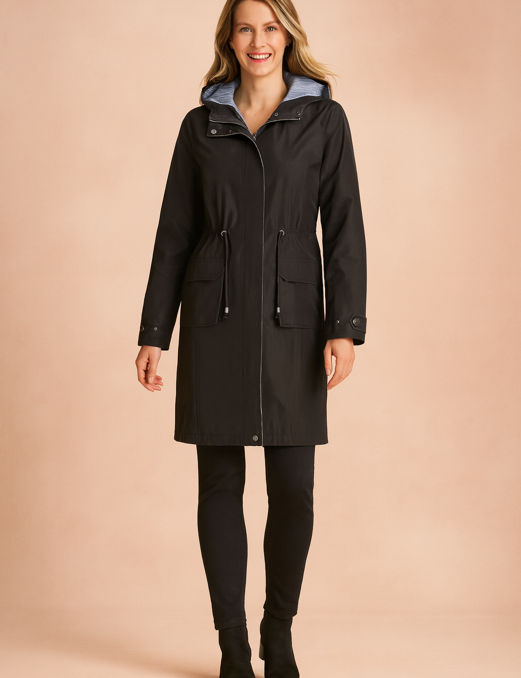 Black waterproof parka with drawstring waist, front snap buttons, large flap pockets, and a light blue hood lining, paired with fitted black pants and ankle boots.