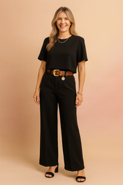 Elegant two-piece black coord set featuring a boxy cropped short-sleeve top and wide-leg tailored pants, accentuated with a chunky brown belt and gold coin charm, styled for a chic and polished look.