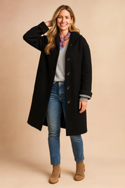 Black button-up wool coat with a relaxed fit, long sleeves, front buttons, and side pockets styled over a grey top, blue jeans, and beige ankle boots.