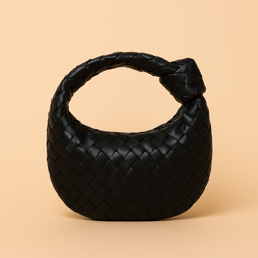 Black woven leather hobo handbag with a crescent shape and knotted handle, displayed against a warm sand and pastel pink gradient background.