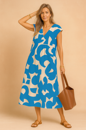 Elegant European woman in a blue and beige abstract print midi summer dress with V-neckline.