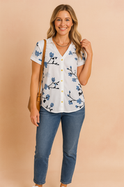 White button-front blouse with blue floral print and folded cuff sleeves, styled with medium-wash jeans and white sneakers for a casual, polished look.