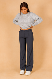High-waisted blue-gray tailored trousers with clean front seam detail, styled with a light gray cable-knit cropped sweater and paired with classic white sneakers for a casual polished look.

