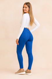 Blue ribbed-knee jeggings styled with a fitted white crop top and taupe sneakers, captured from behind in a fashion shoot with pastel sand-pink background