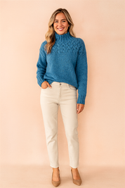 Blue cable-knit high-neck sweater paired with off-white straight-leg pants and beige pointed-toe heels.