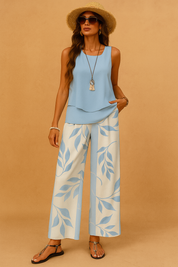 Light blue sleeveless top paired with wide-leg cream trousers featuring soft blue leaf patterns, styled with black sandals and summer accessories for a breezy and elegant daytime look.