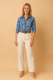Blue button-up shirt with bold white abstract print, tucked into tailored ivory pants, accessorized with a brown belt and gold buckle.