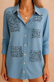 Light blue button-down shirt with black handwritten script print, featuring front buttons, long sleeves, and a chest pocket; elegant casualwear with artistic calligraphy pattern for a modern statement look.