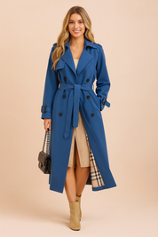 Elegant long blue trench coat with double-breasted design, waist belt, and detailed plaid inner lining, styled with classic buttons and structured shoulders.