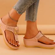 Blush pink wedge sandals with perforated straps and gold buckle accents, featuring a cushioned insole and beige sole designed for a stylish, casual look.
