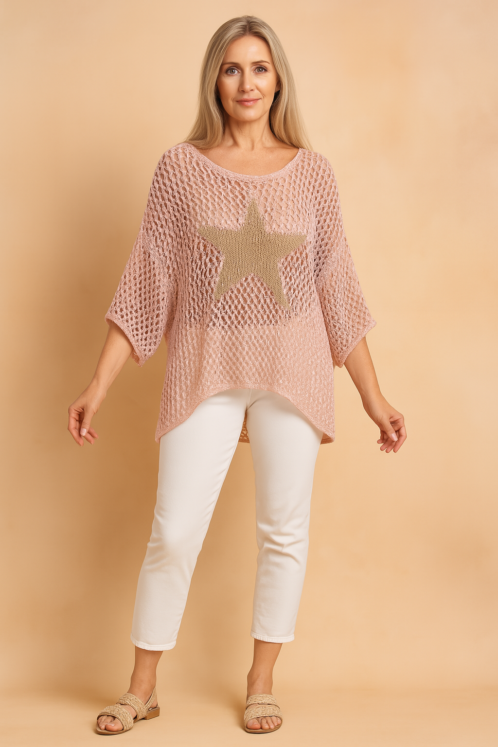Pastel pink oversized open-knit blouse with a beige star pattern on the front, styled with white cropped pants and beige sandals in a fashion-forward, casual ensemble.