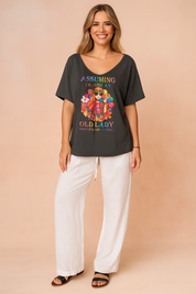 Dark gray oversized T-shirt with a colorful bohemian-style graphic and statement text, paired with loose white drawstring pants and black sandals for a relaxed, bold look.